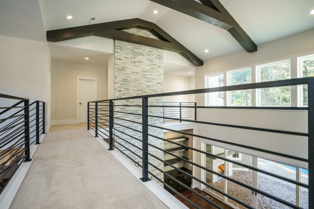 Upper floor of a warm modern home containing wooden beams and wrought-iron horizontal stair rail.